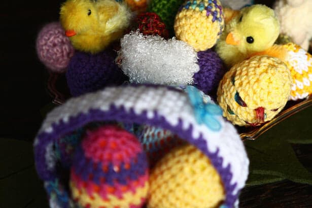 A basket of colorful knitted Easter eggs and fluffy chick decorations. - Home Instead