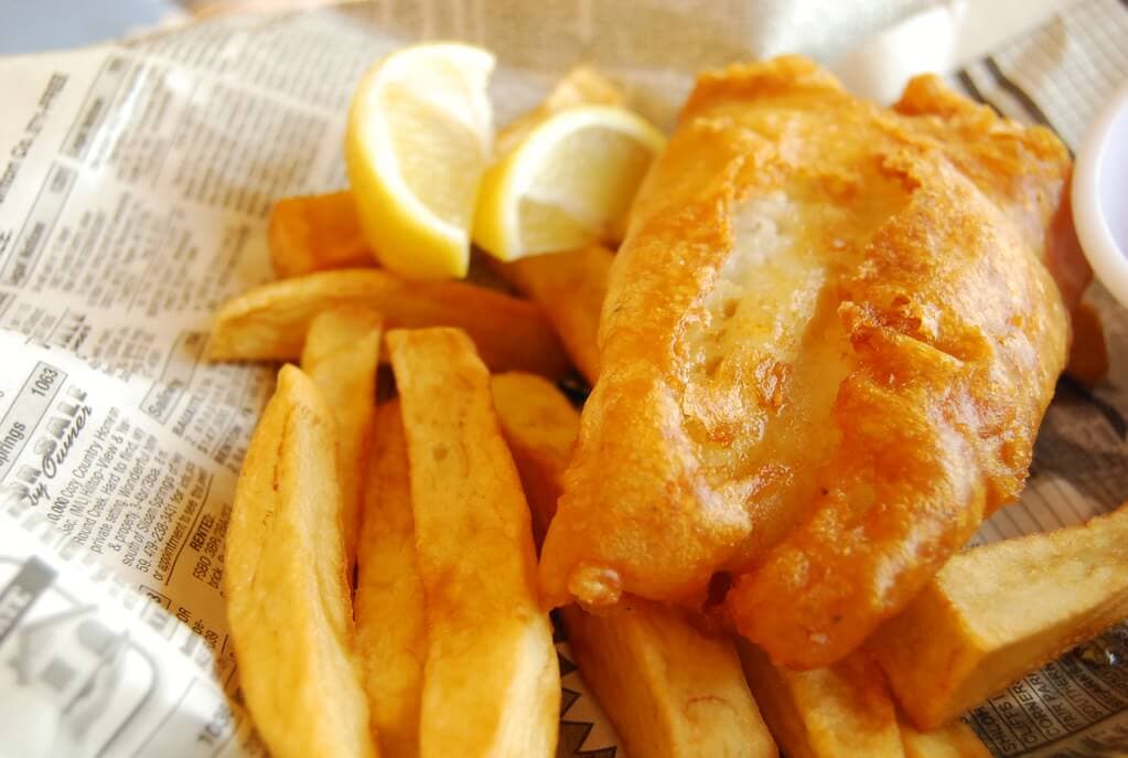 A serving of fish and chips with lemon wedges on a piece of newspaper. - Home Instead