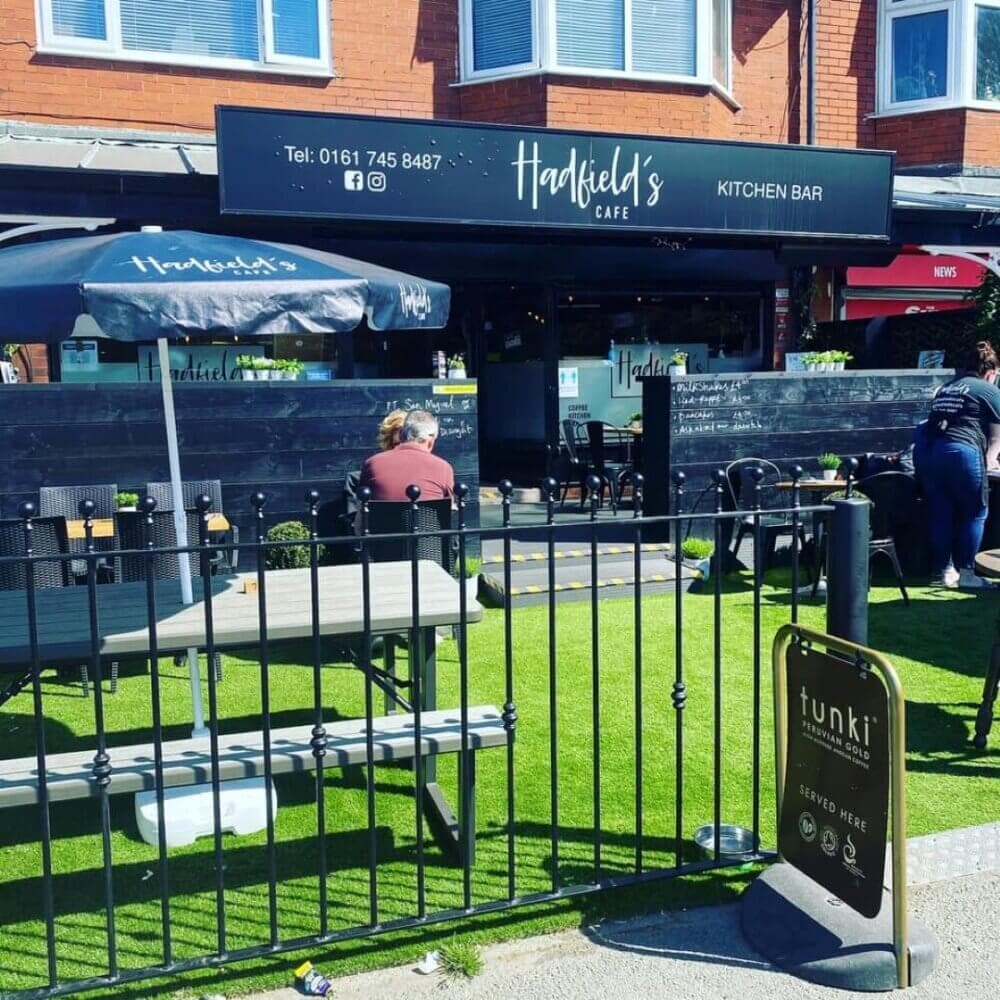 Outdoor seating at Hatfield's Cafe with people dining, fenced garden area, and a signboard for Tunki coffee blend. - Home Instead