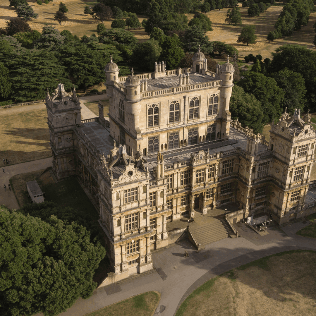 Aerial view of a grand historic mansion with ornate architecture, surrounded by trees and greenery on a sunny day. - Home Instead