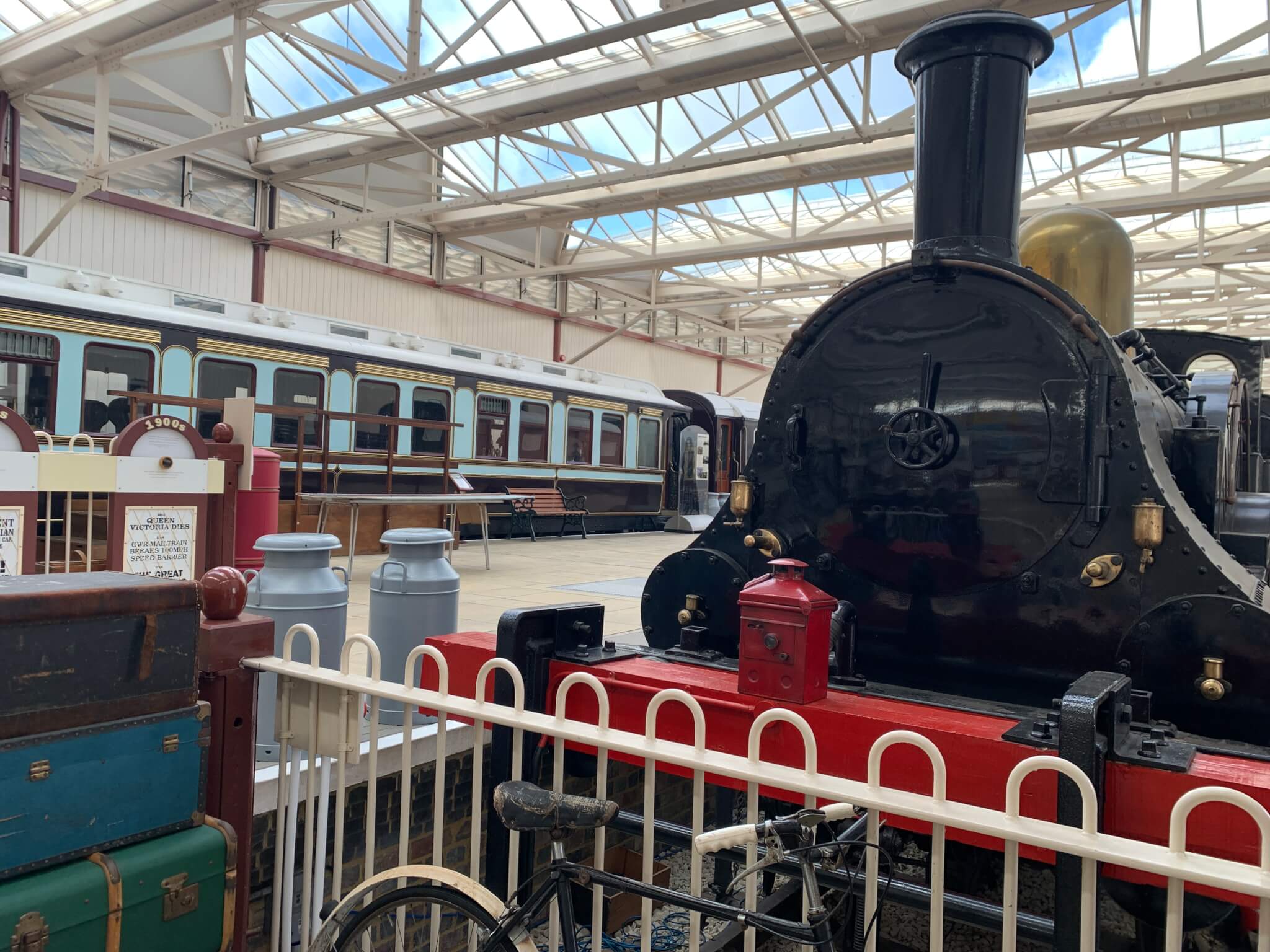 A vintage black steam locomotive displayed indoors, with old-fashioned suitcases and a bicycle in the foreground. - Home Instead