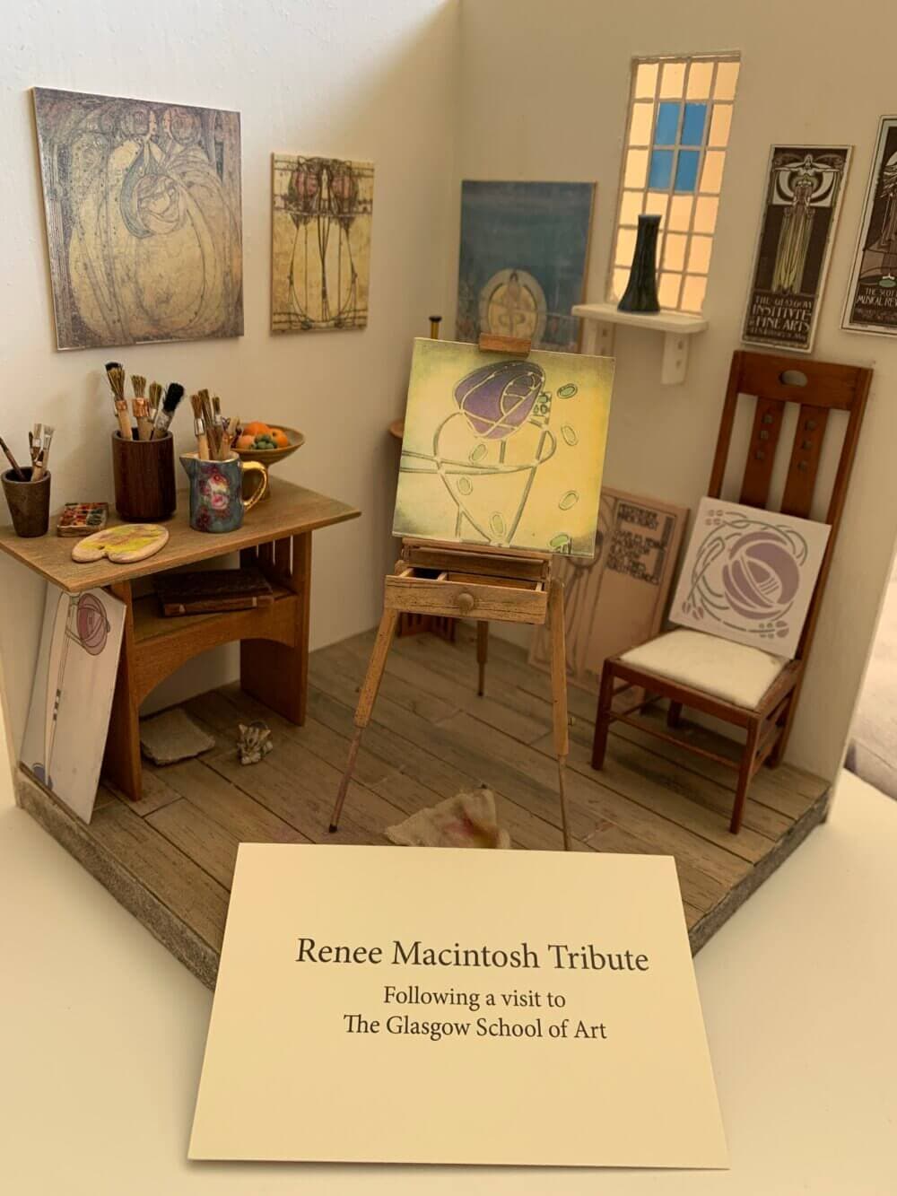 Miniature art studio set up as a tribute to Renee Mackintosh, featuring an easel, paintings, and art supplies. - Home Instead