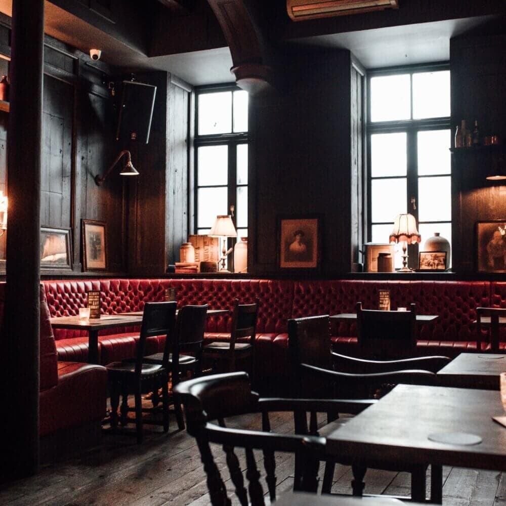 Cozy pub interior with red leather booth seating, wooden tables, chairs, and framed pictures on dark walls. - Home Instead