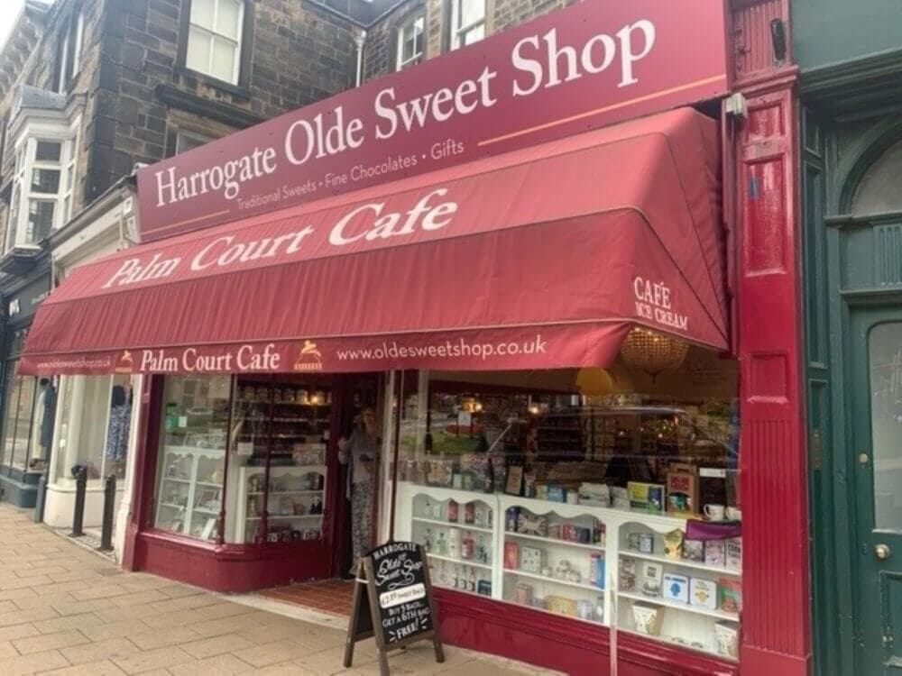 Front view of Harrogate Olde Sweet Shop with red awning, next to Palm Court Cafe; display window full of sweets. - Home Instead