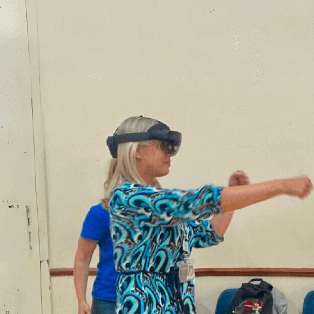 A woman wearing a virtual reality headset, extending her arms while engaging with the VR experience. - Home Instead