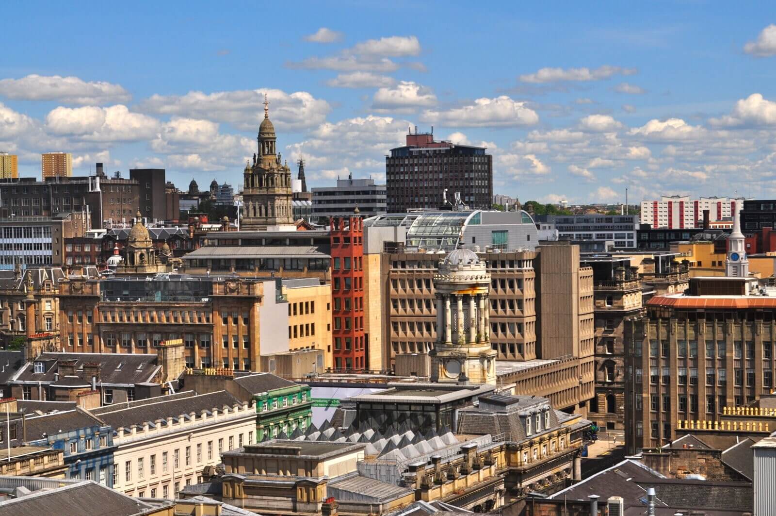 Aerial view of a cityscape with historic and modern buildings under a partly cloudy blue sky. - Home Instead