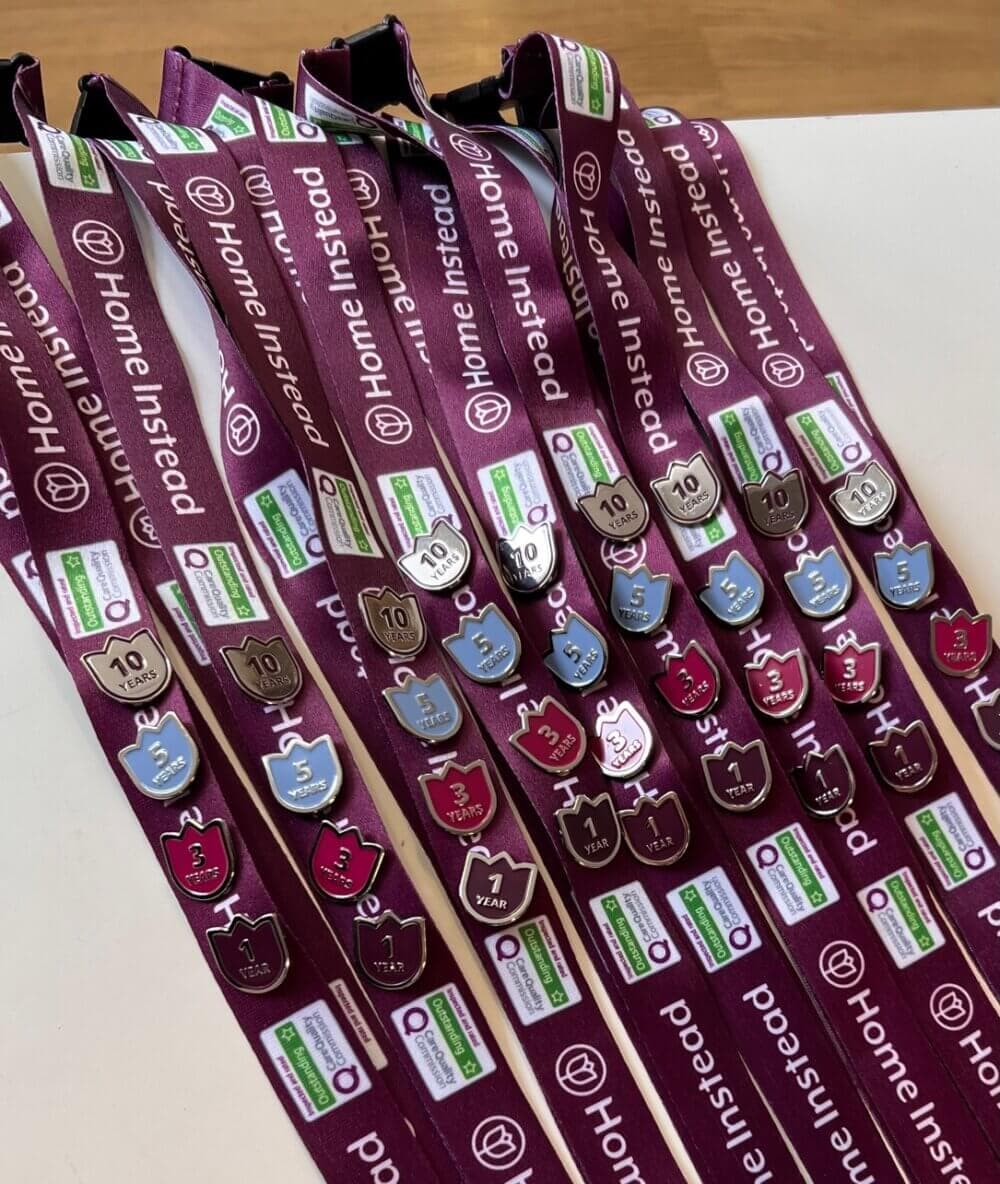 Multiple maroon lanyards with various milestone pins displayed on a flat surface, featuring "Home Instead" branding. - Home Instead