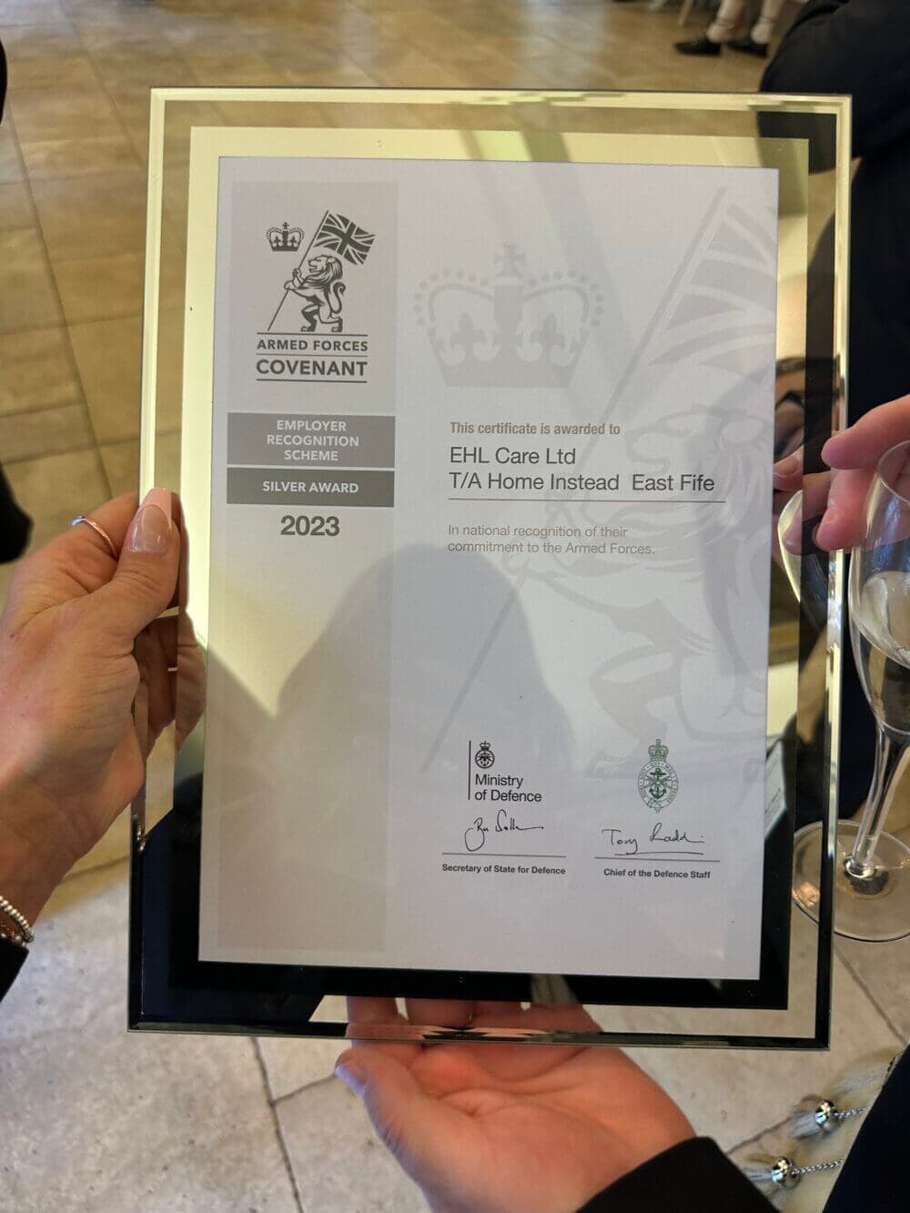A person holds a framed certificate awarded to EHL Care Ltd for Armed Forces Covenant Silver Award 2023. - Home Instead