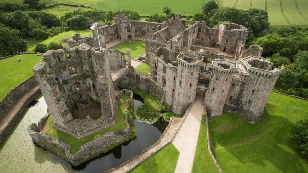Aerial view of a vast, medieval stone castle with towers, surrounded by a moat and lush green fields. - Home Instead