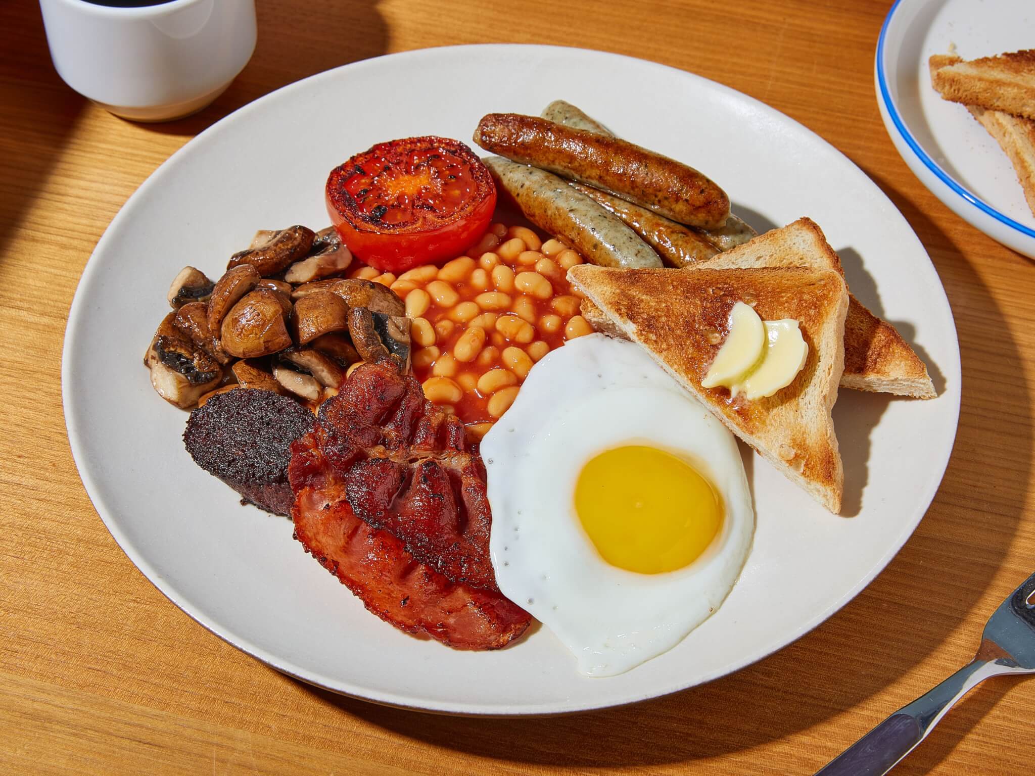 A plate with an English breakfast: egg, bacon, sausages, baked beans, mushrooms, grilled tomato, black pudding, and toast. - Home Instead