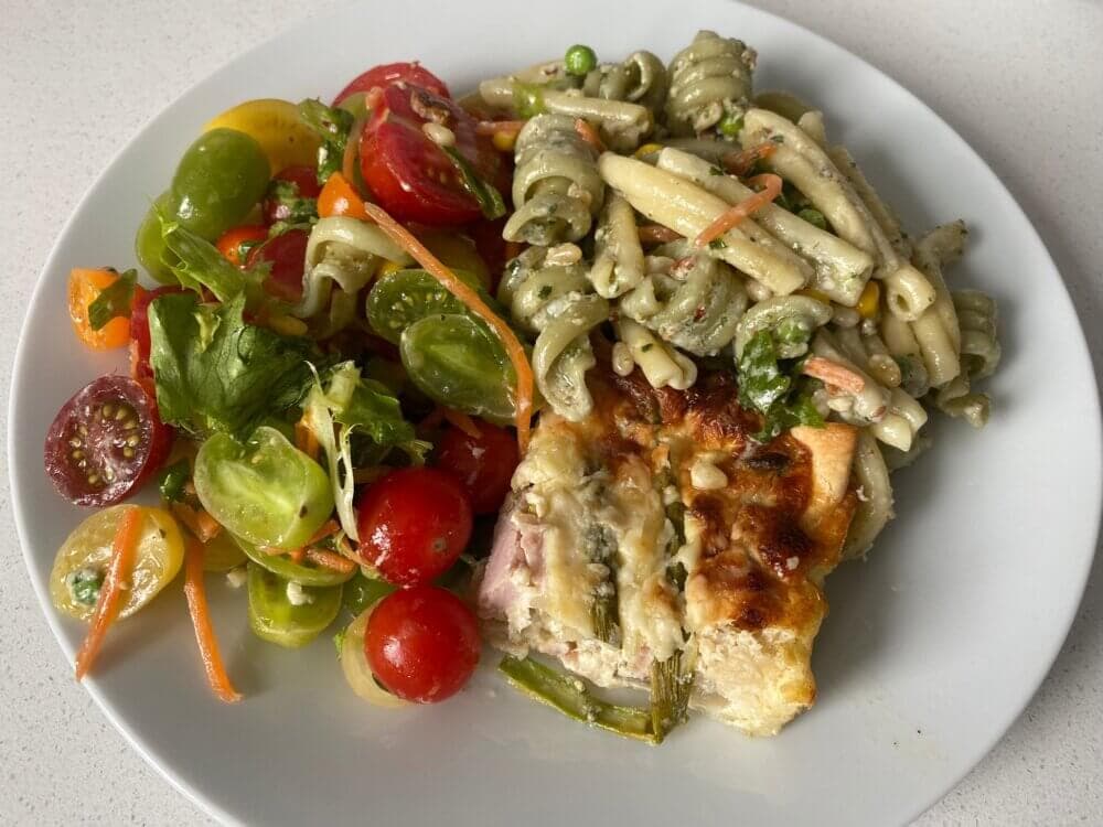 A plate with assorted salad of cherry tomatoes, mixed greens, and pasta salad next to a portion of quiche. - Home Instead