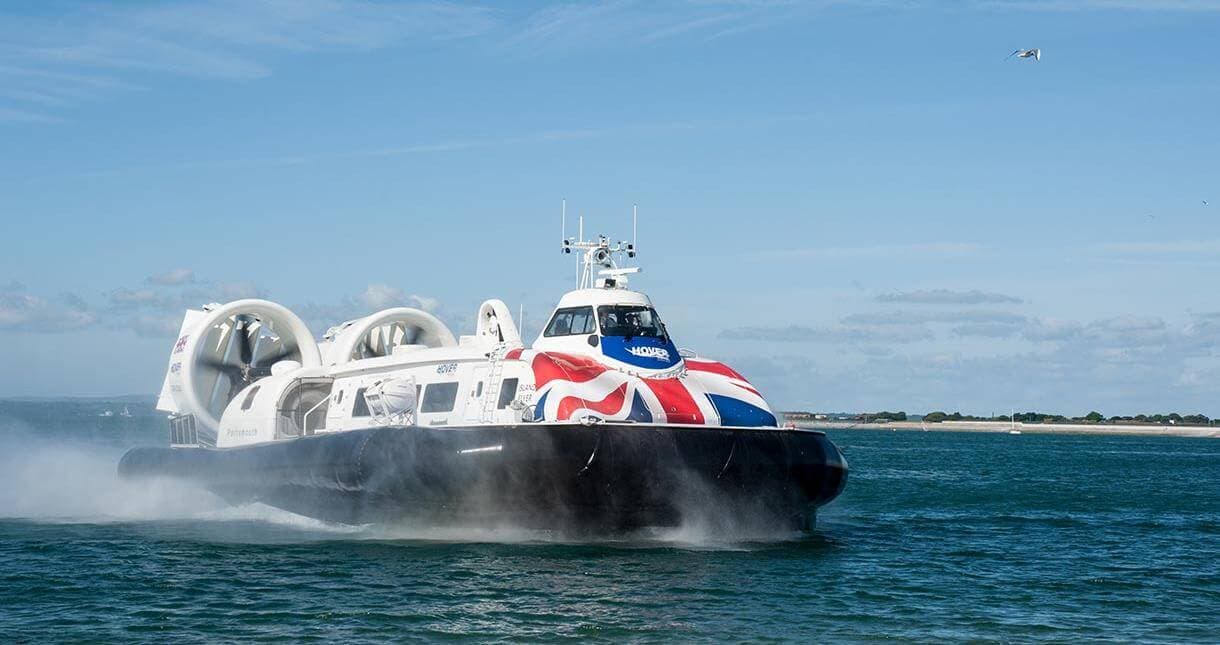 A hovercraft with a Union Jack design glides over the water on a sunny day with a seagull flying overhead. - Home Instead