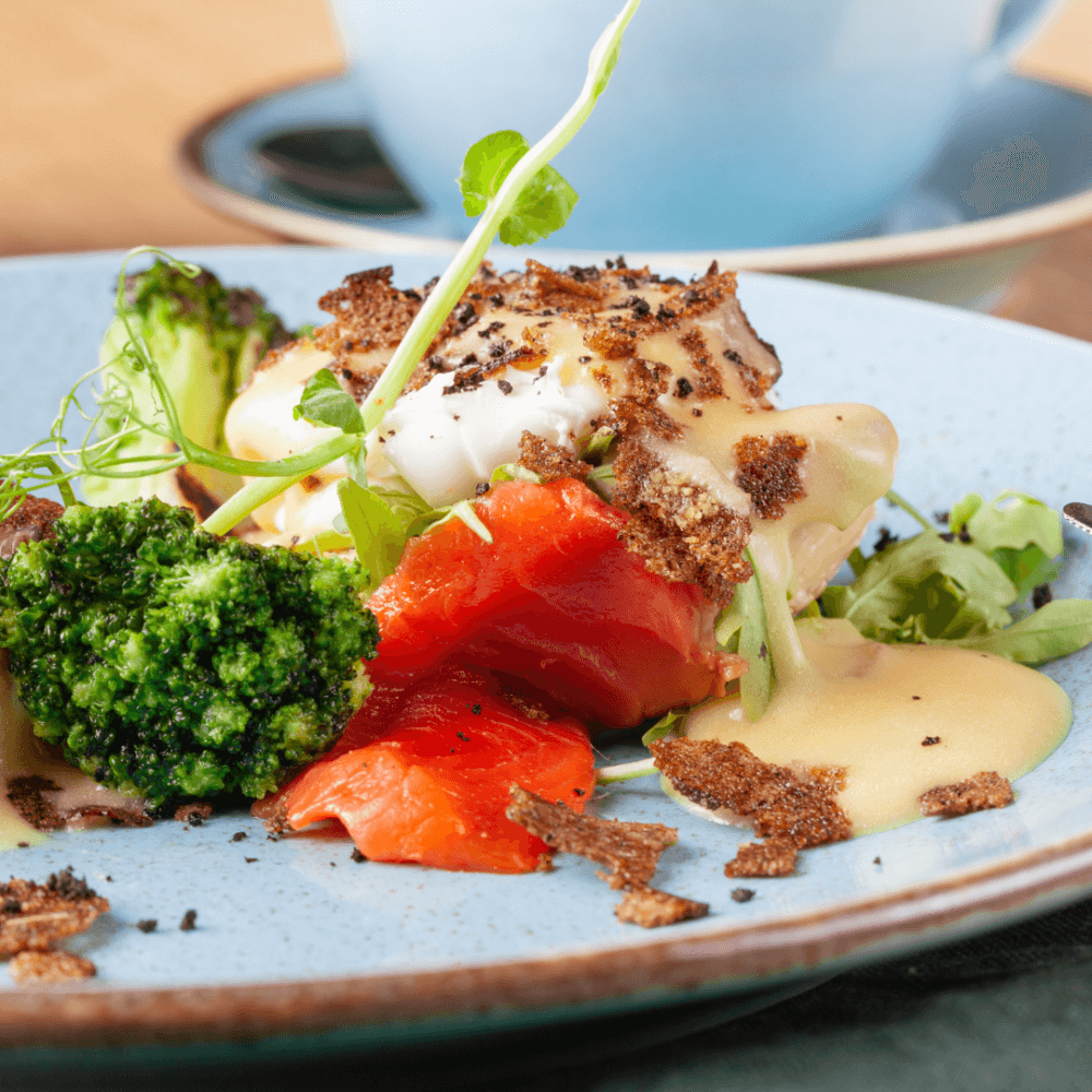 A plated dish featuring broccoli, red peppers, a poached egg topped with sauce, and garnished with fresh greens. - Home Instead