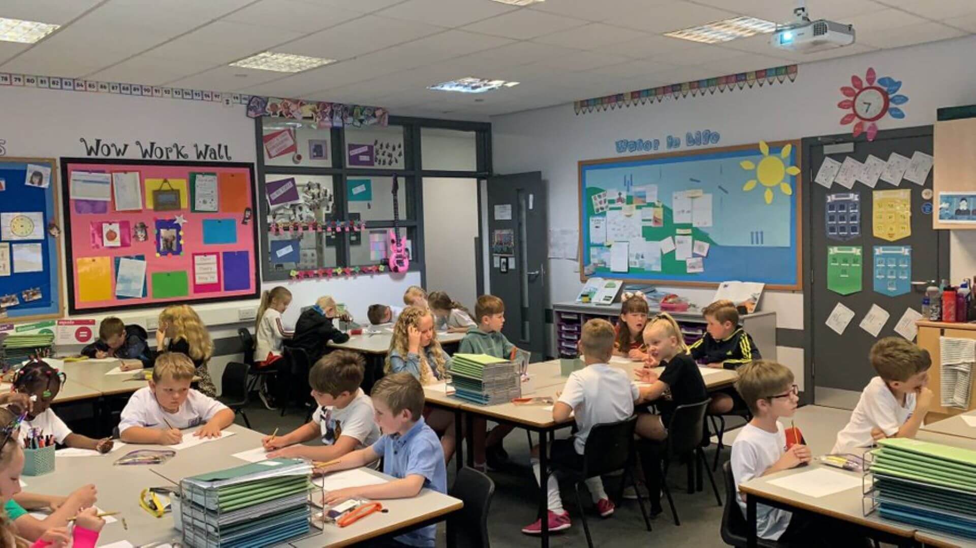 A classroom of young students working on different tasks at their desks, with colorful decorations on the walls. - Home Instead
