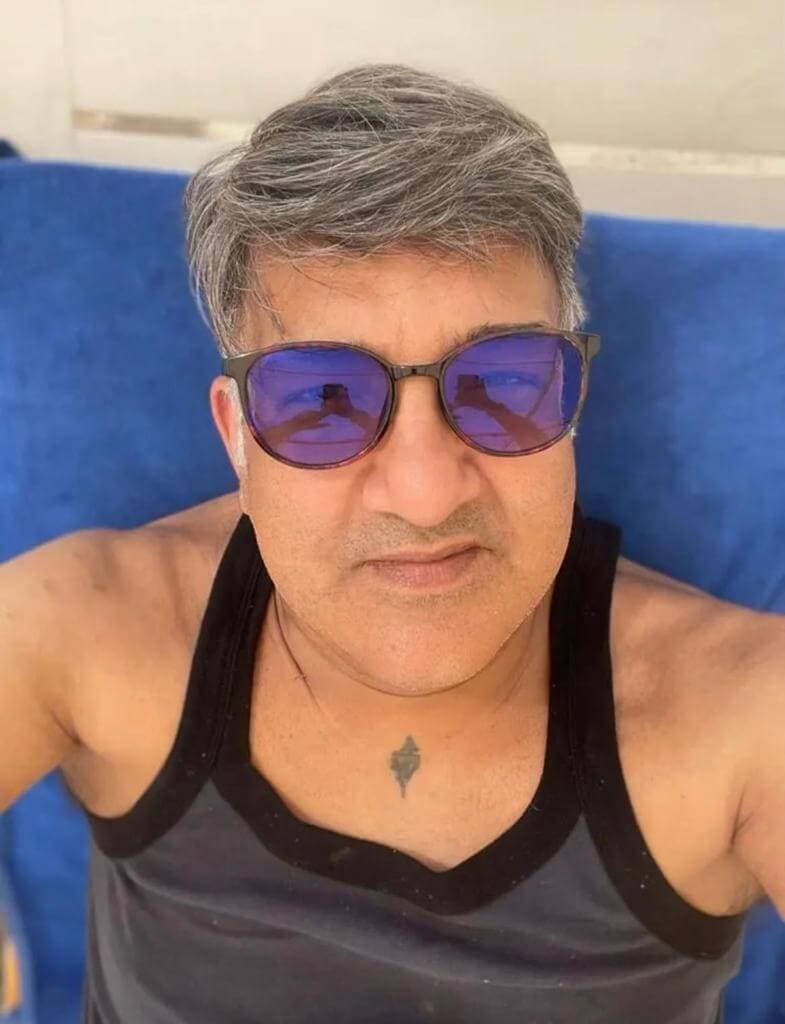 Man in a black tank top wearing blue sunglasses, looking at the camera with a neutral expression. - Home Instead