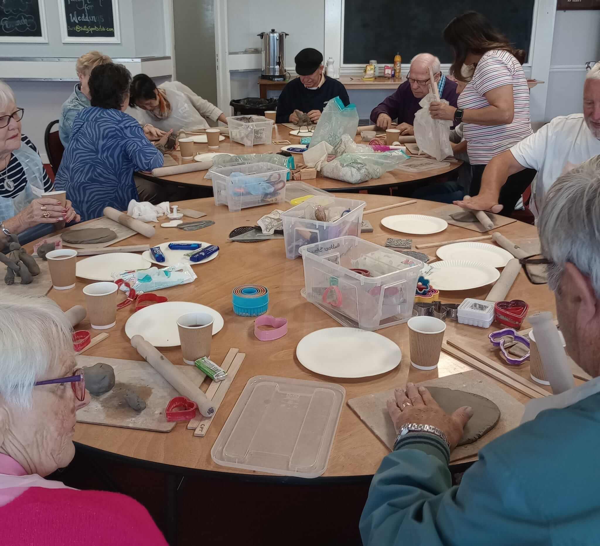 A group of people engaging in a craft activity around a table, with clay and various crafting tools. - Home Instead