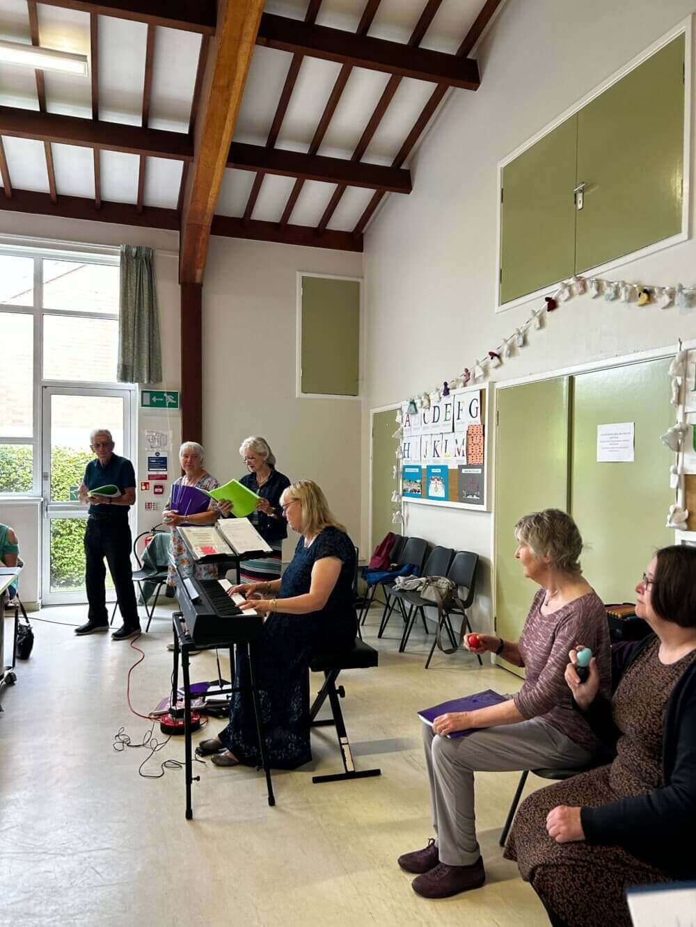 A group of people performing music indoors, with a keyboard player and other members holding musical instruments and singing. - Home Instead