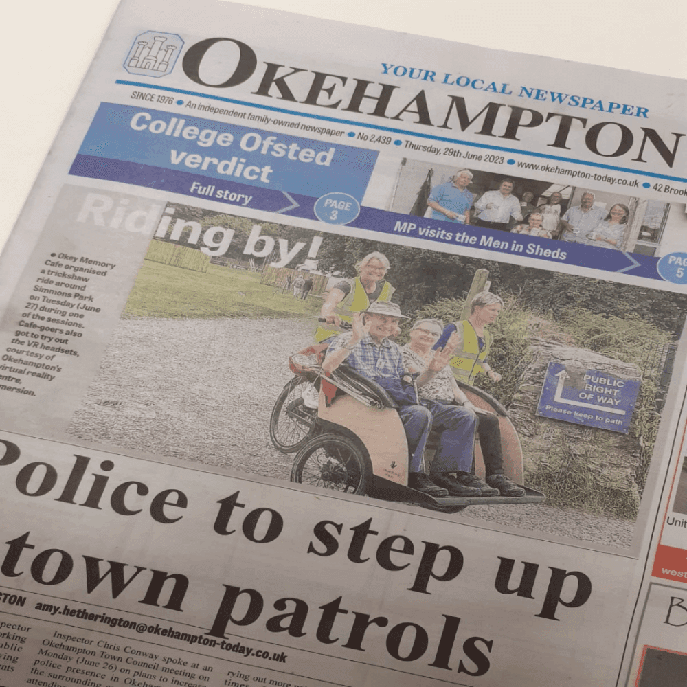 People ride in a bicycle-pulled cart on the cover of the Okehampton newspaper under the headline "Riding by!. - Home Instead