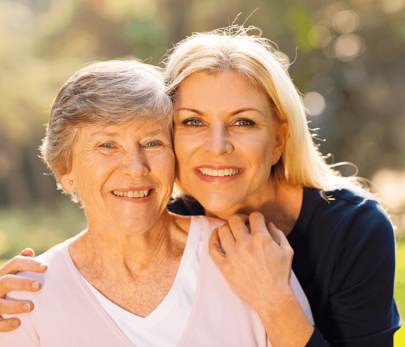 Two women smiling outdoors, one with short gray hair in a pink top, and the other with long blonde hair in a black top. - Home Instead