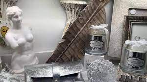 White statue, candle jars, silver clutch, and a decorative leaf in a stylish display with a textured white background. - Home Instead