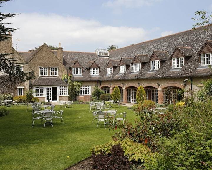 A building with many windows and a sloped roof, featuring an outdoor area with tables and chairs on a green lawn. - Home Instead
