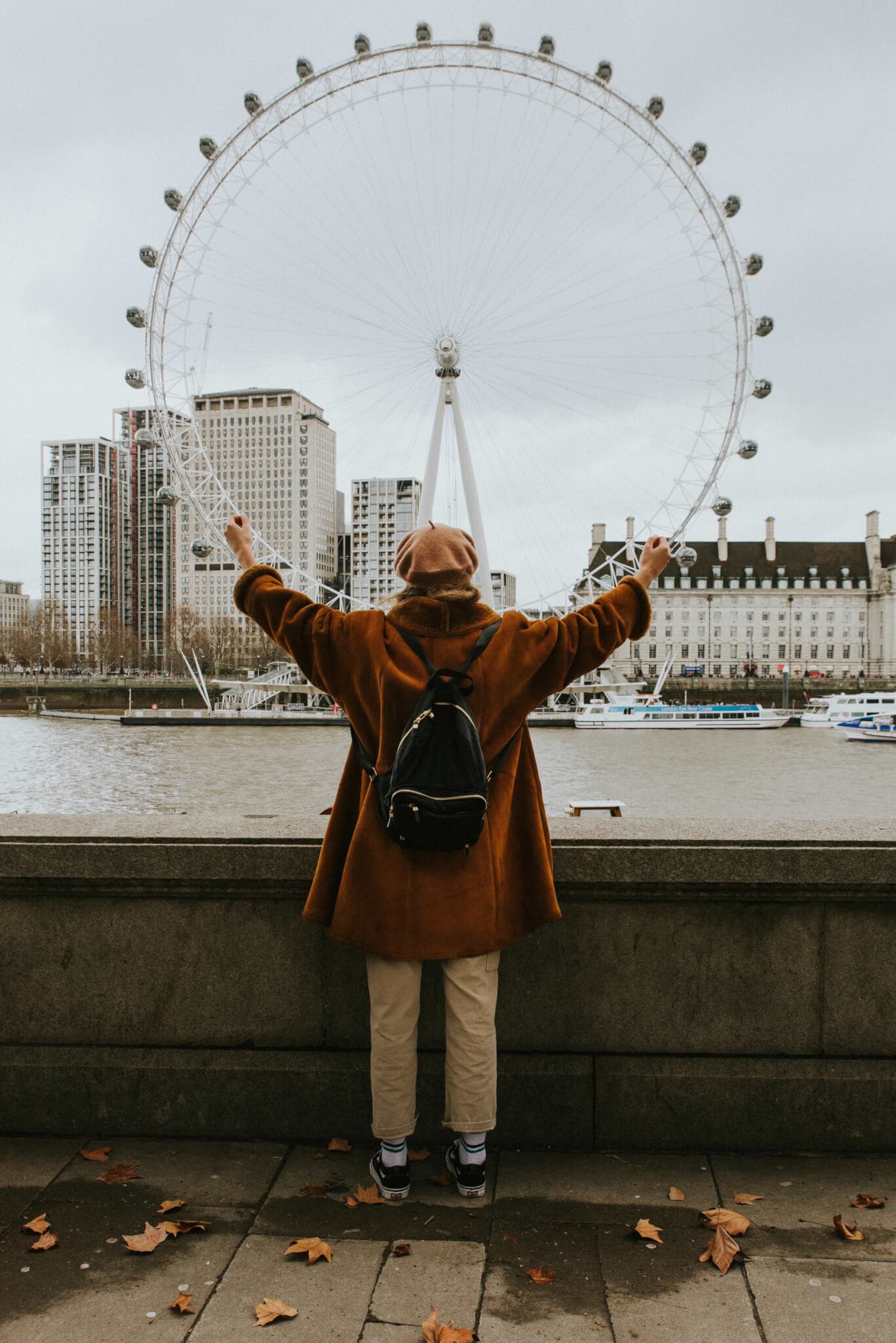 Person with arms outstretched facing the London Eye, standing by a riverside with buildings in the background. - Home Instead