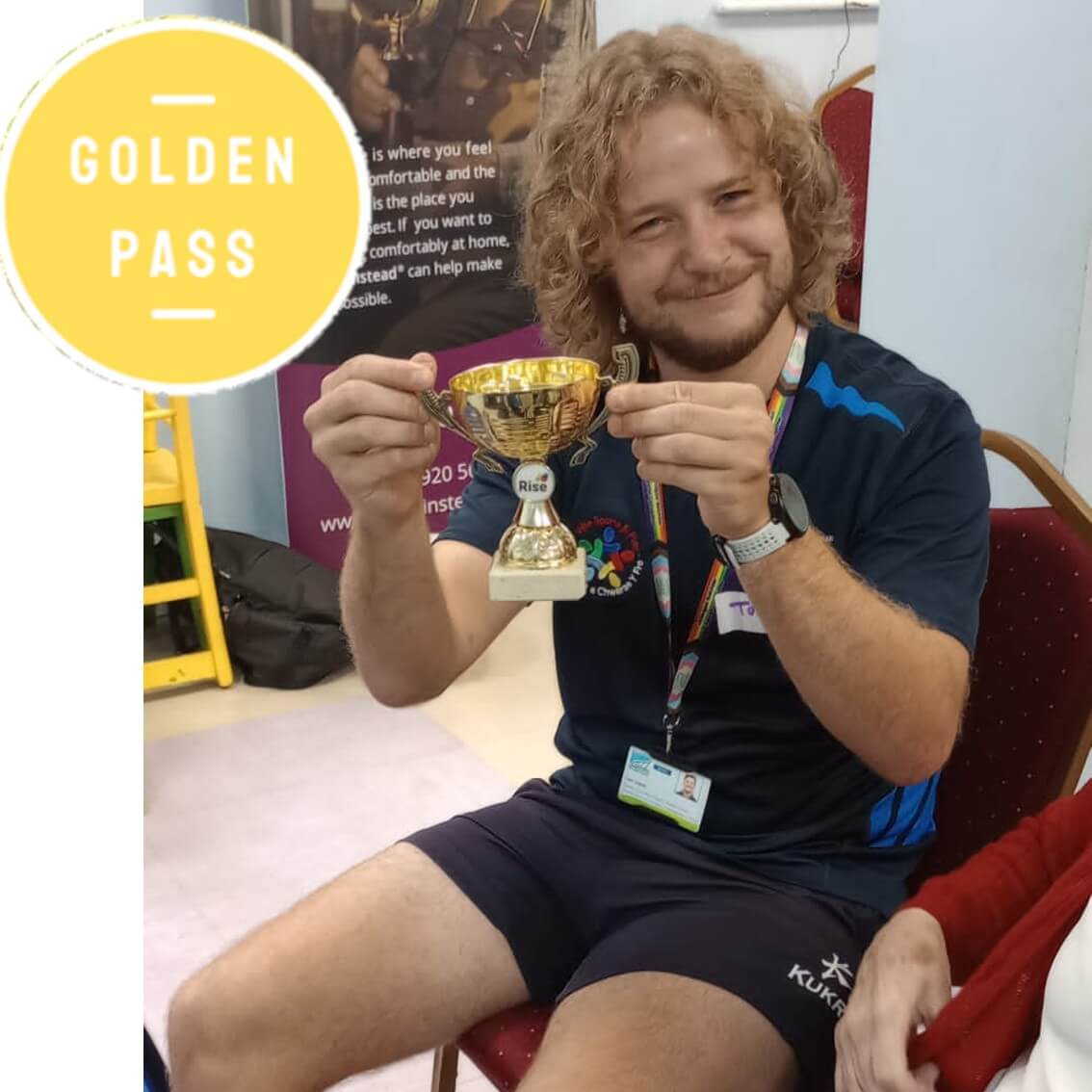 A person with curly hair smiles, holding a gold trophy. A circular "GOLDEN PASS" emblem is in the top left corner. - Home Instead