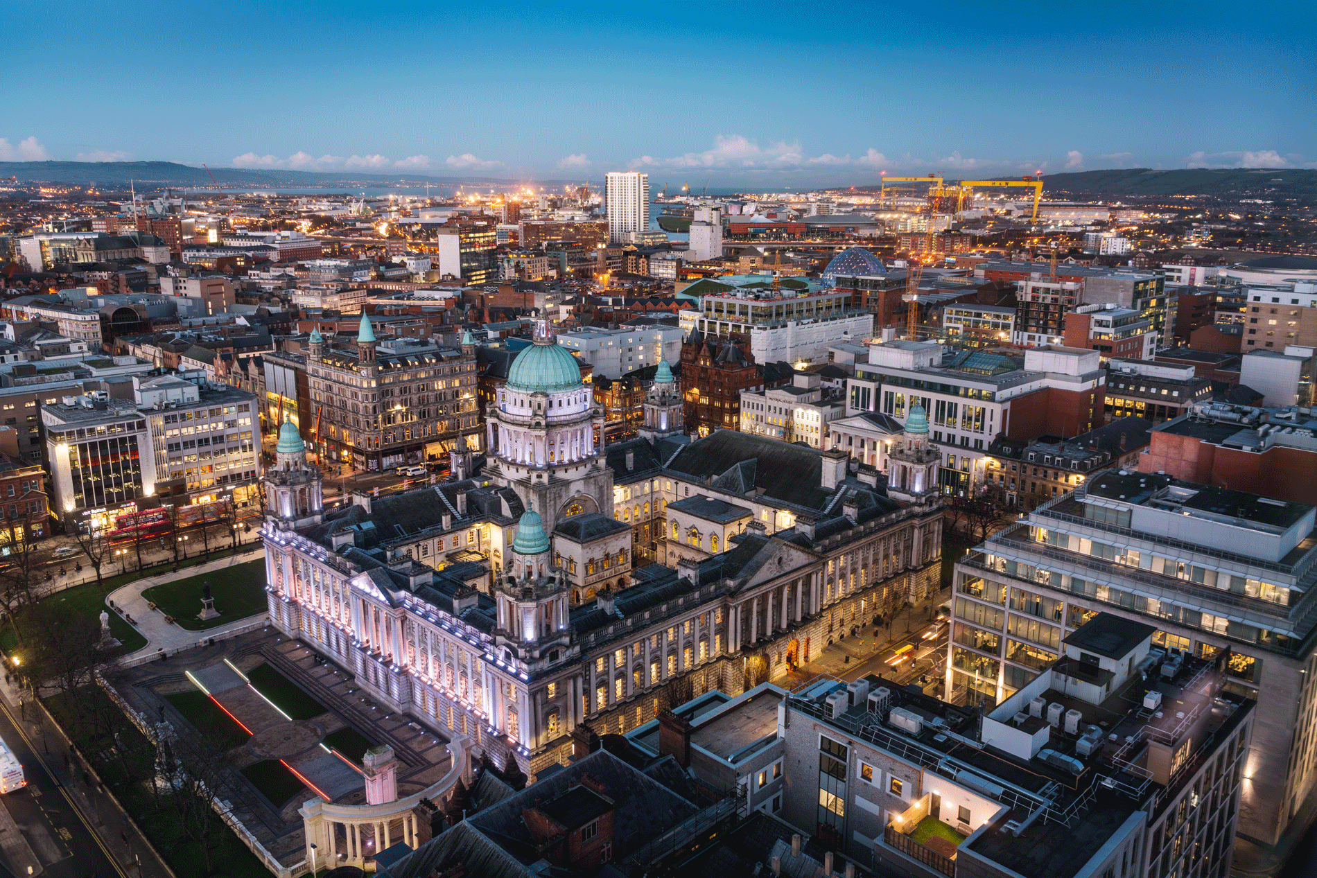 Aerial view of Belfast cityscape at dusk, highlighting Belfast City Hall with lights and surrounding buildings. - Home Instead