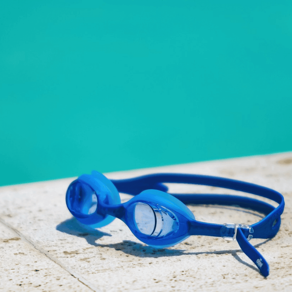 Blue swimming goggles rest on the edge of a pool with clear turquoise water in the background. - Home Instead