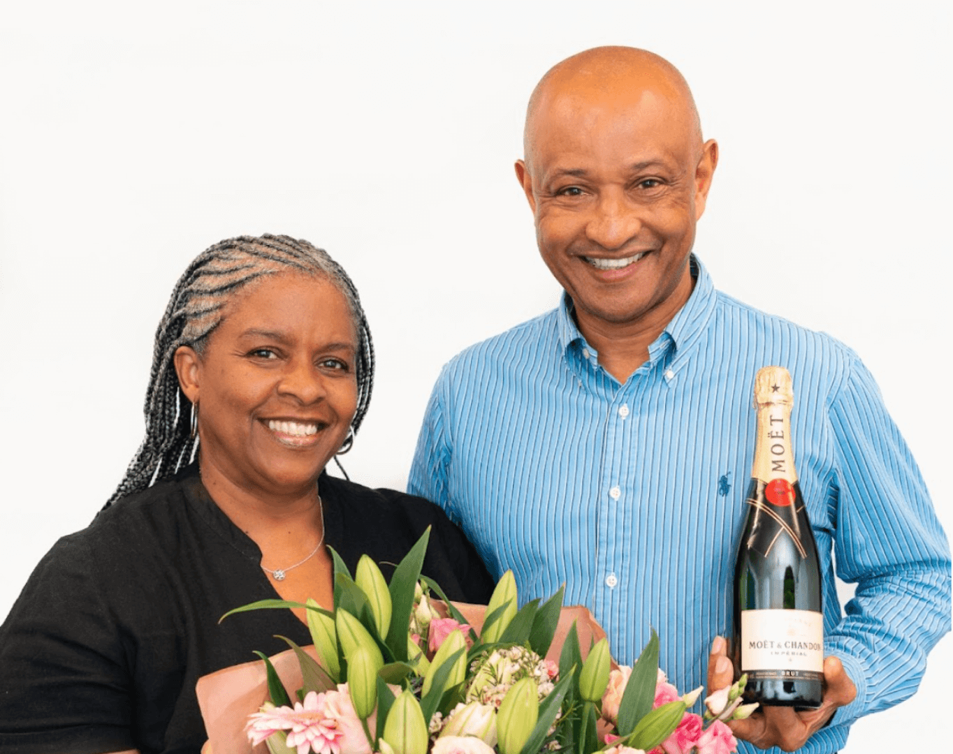 Two people smiling; the woman holding a bouquet, the man holding a bottle of champagne. - Home Instead