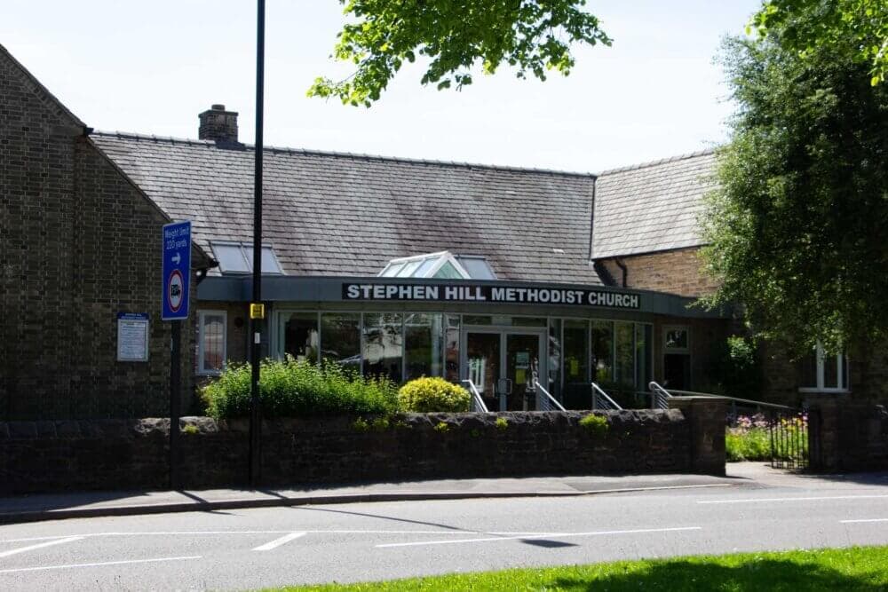 Exterior of Stephen Hill Methodist Church with a glass entrance, brick walls, and surrounding greenery. - Home Instead