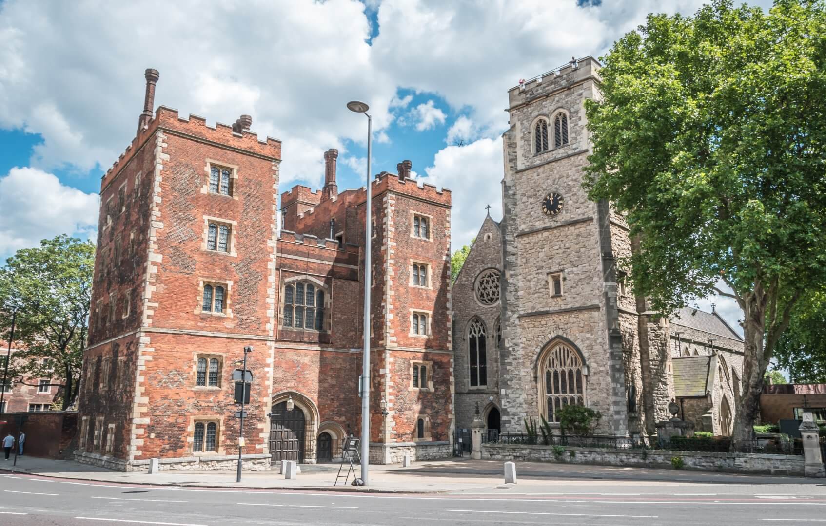 Historic brick and stone buildings with towers and arched windows under a bright, partly cloudy sky. - Home Instead