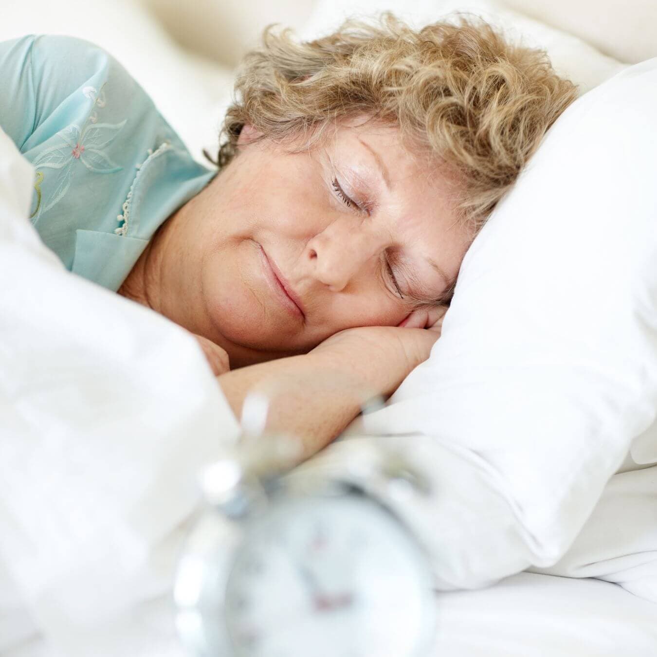 Elderly woman peacefully sleeping in bed with an alarm clock in the foreground. - Home Instead