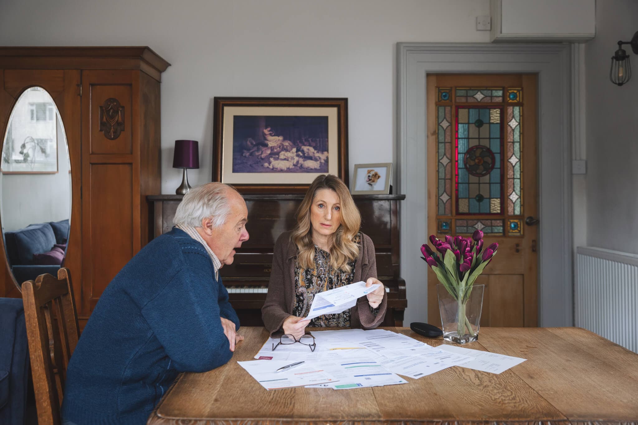 Two people sitting at a table, reviewing documents, in a cozy room with stained glass door and flowers on the table. - Home Instead