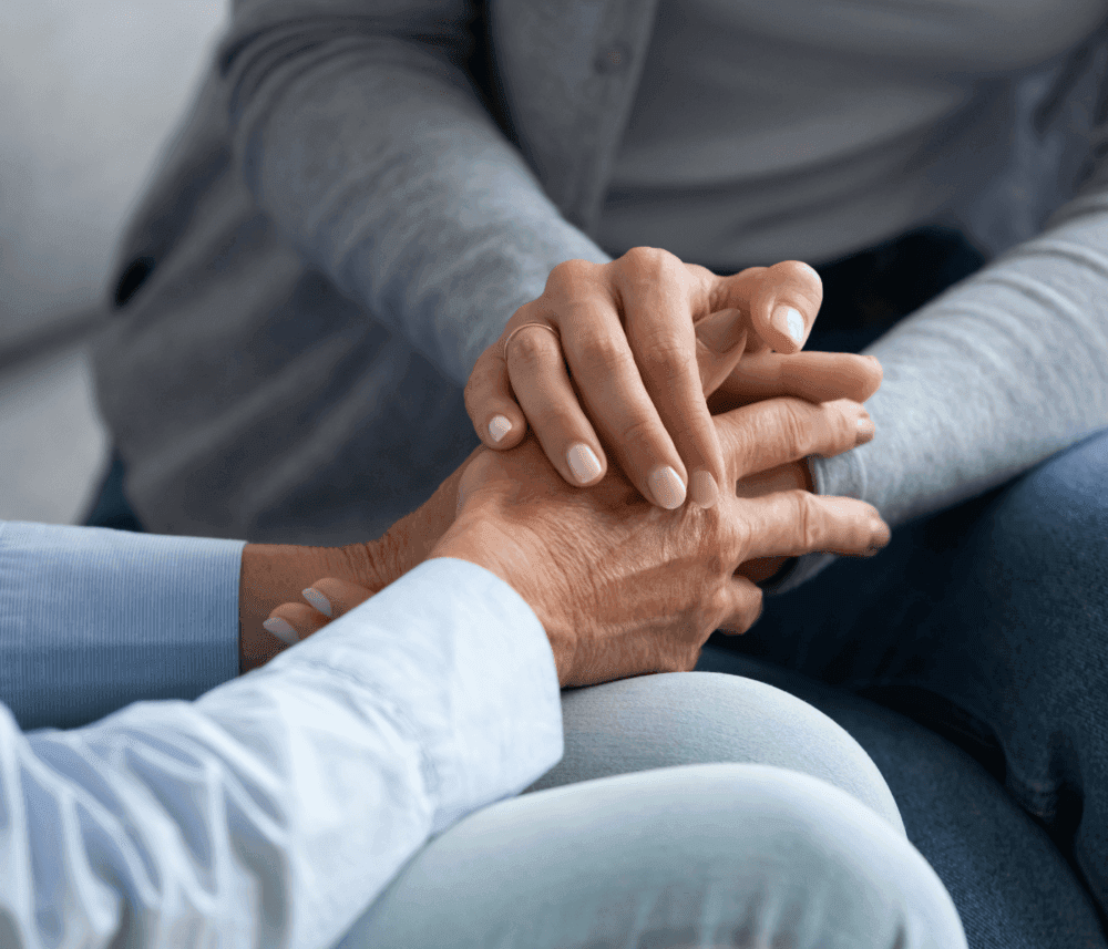 Close-up of two people sitting, one gently holding the other's hand, providing comfort and support. - Home Instead