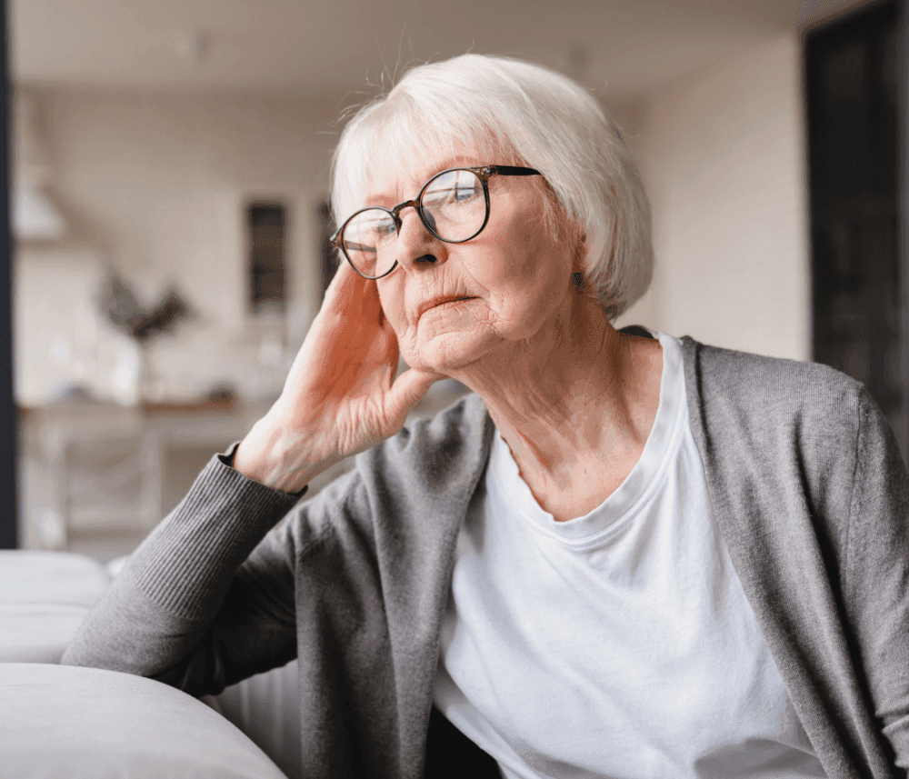Elderly woman with glasses, resting her head on her hand, looking thoughtful while seated indoors. - Home Instead