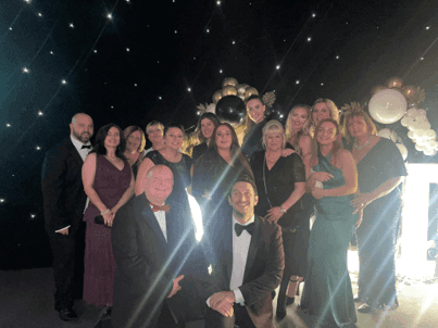 Group of people in formal attire posing together at a fancy event with a decorative background. - Home Instead