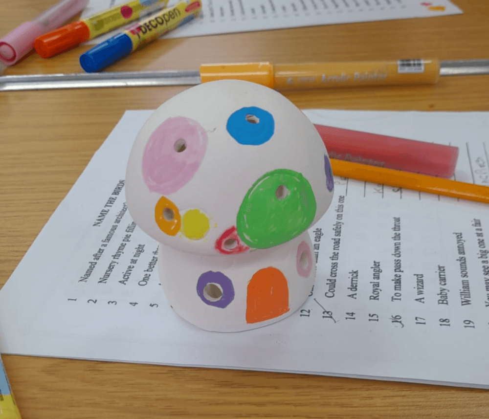 Painted mushroom-shaped ceramic with colorful polka dots on a paper worksheet. Markers are scattered around. - Home Instead