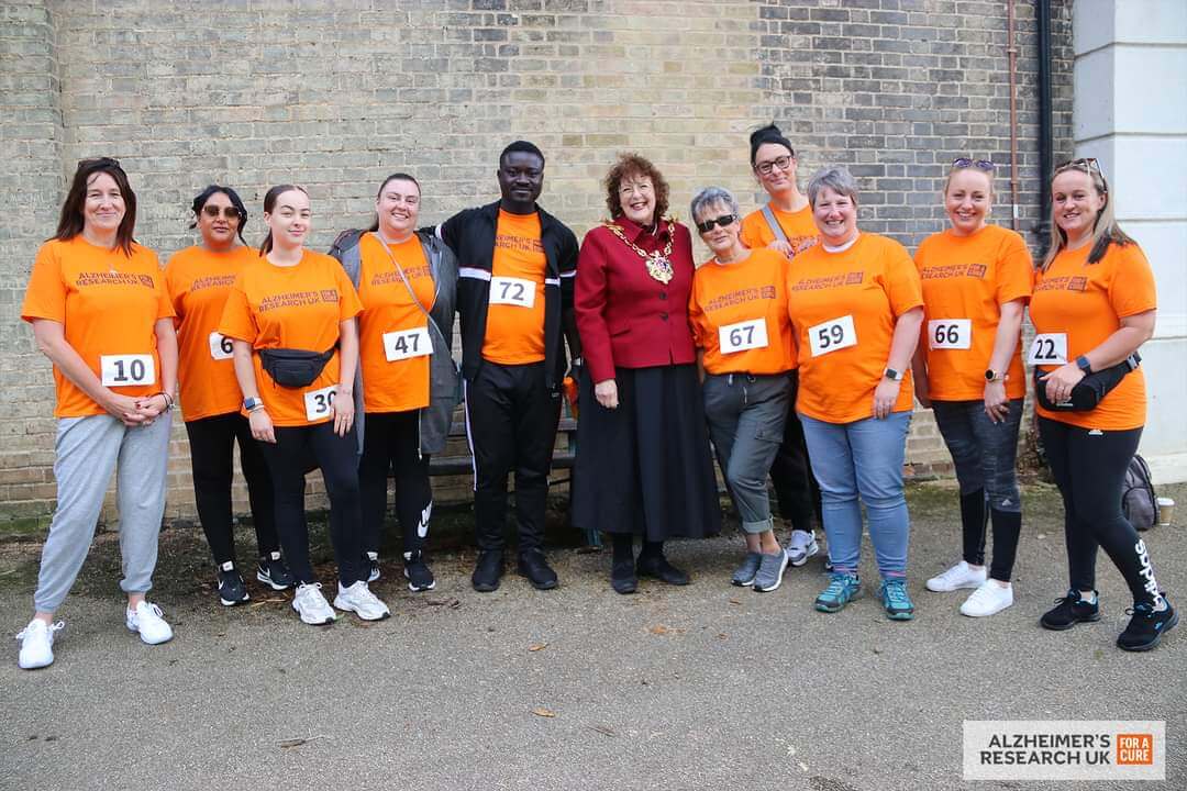 A group of people in sports attire and a woman in official attire pose for a photo at an Alzheimer's Research UK event. - Home Instead