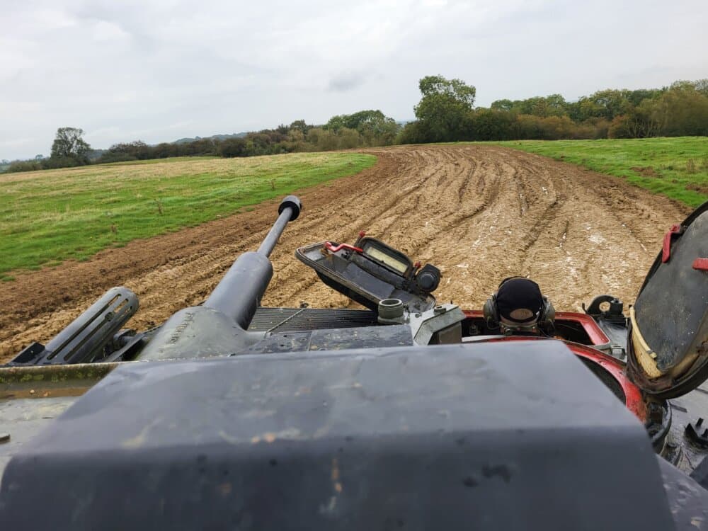 View from a tank cockpit showing a muddy field with a trail and trees in the background on a cloudy day. - Home Instead