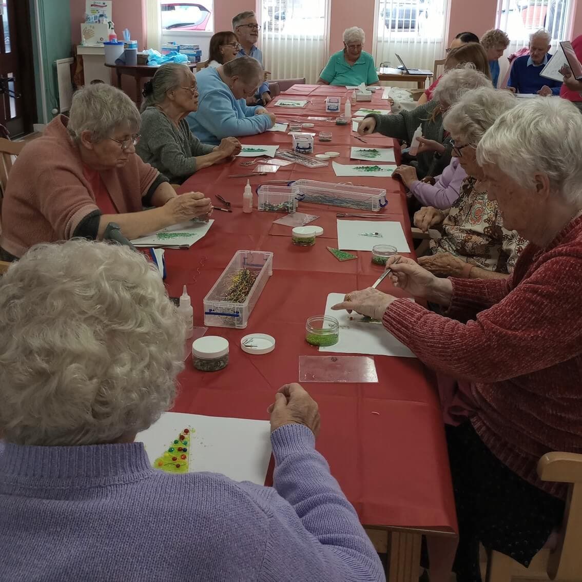 Group of elderly individuals engaged in an arts and crafts session around a table in a community center. - Home Instead