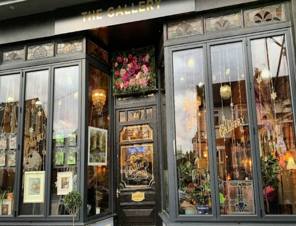 Front view of a small art gallery with floral decorations, large windows displaying artwork, and a black door. - Home Instead
