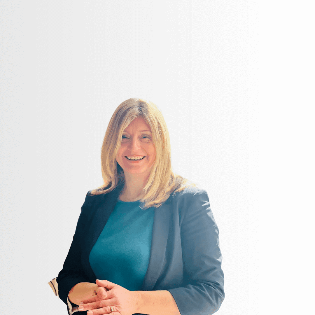 A woman with long blonde hair and a teal shirt, smiling, stands against a white background. - Home Instead