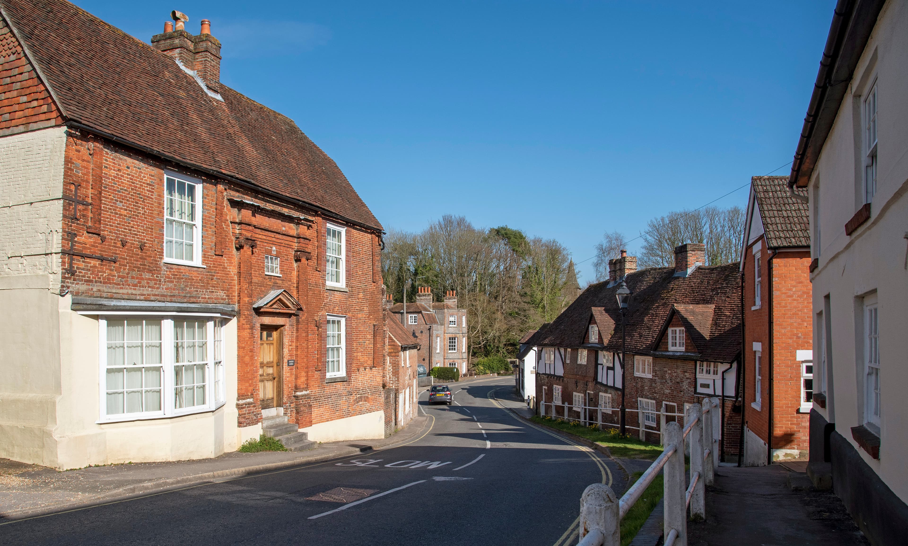 A quiet and sunny street in a small village with charming brick houses and a "SLOW" road marking. - Home Instead