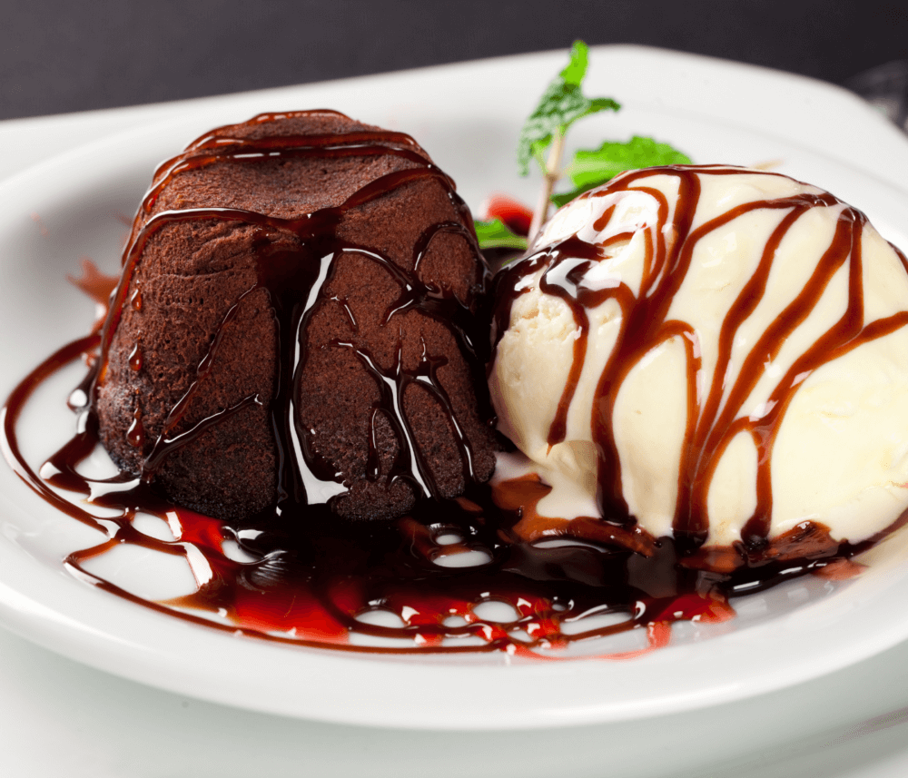 Chocolate lava cake and vanilla ice cream drizzled with chocolate and strawberry sauce on a white plate. - Home Instead