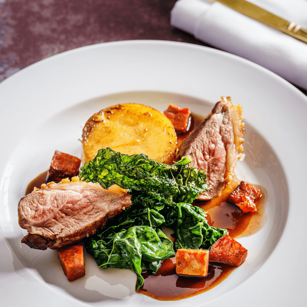 Gourmet dish with medium-rare meat slices, leafy greens, grilled polenta, and roasted vegetables on a white plate. - Home Instead