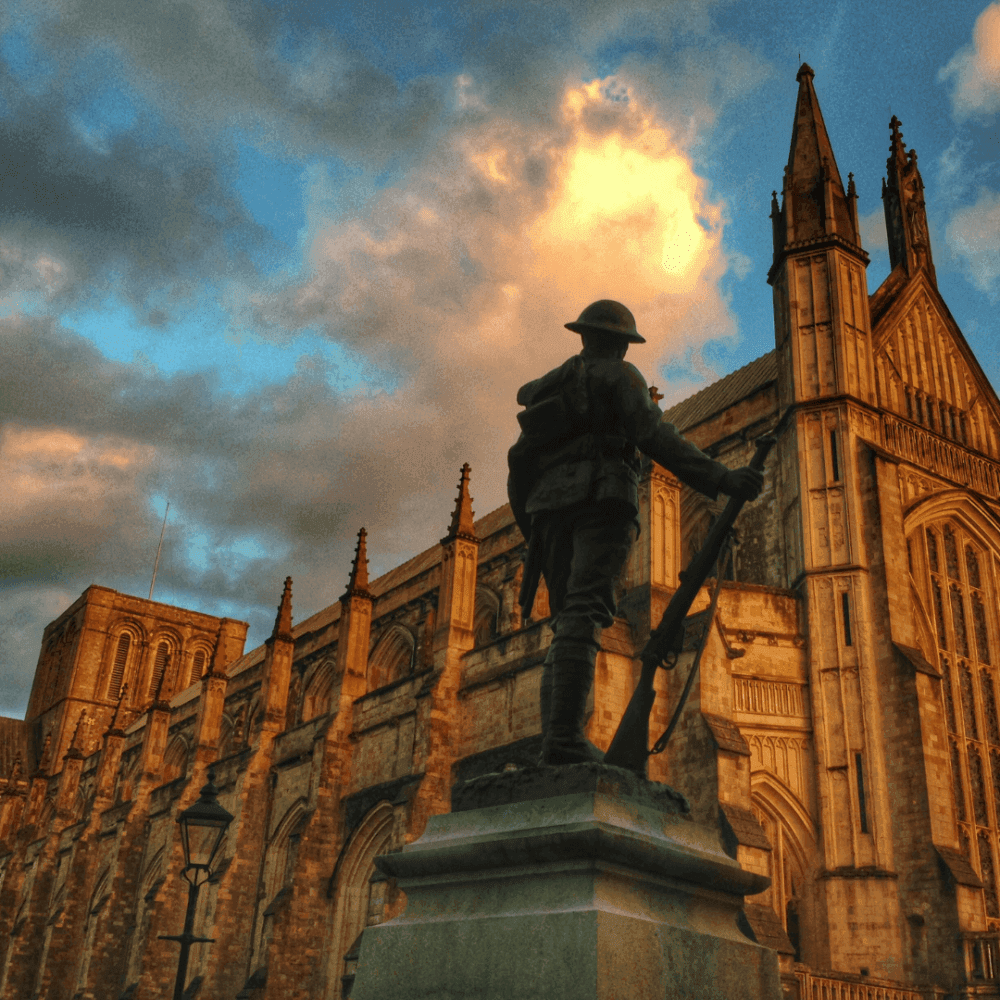 Statue of a soldier in front of a historic cathedral against a dramatic sky with clouds at sunset. - Home Instead