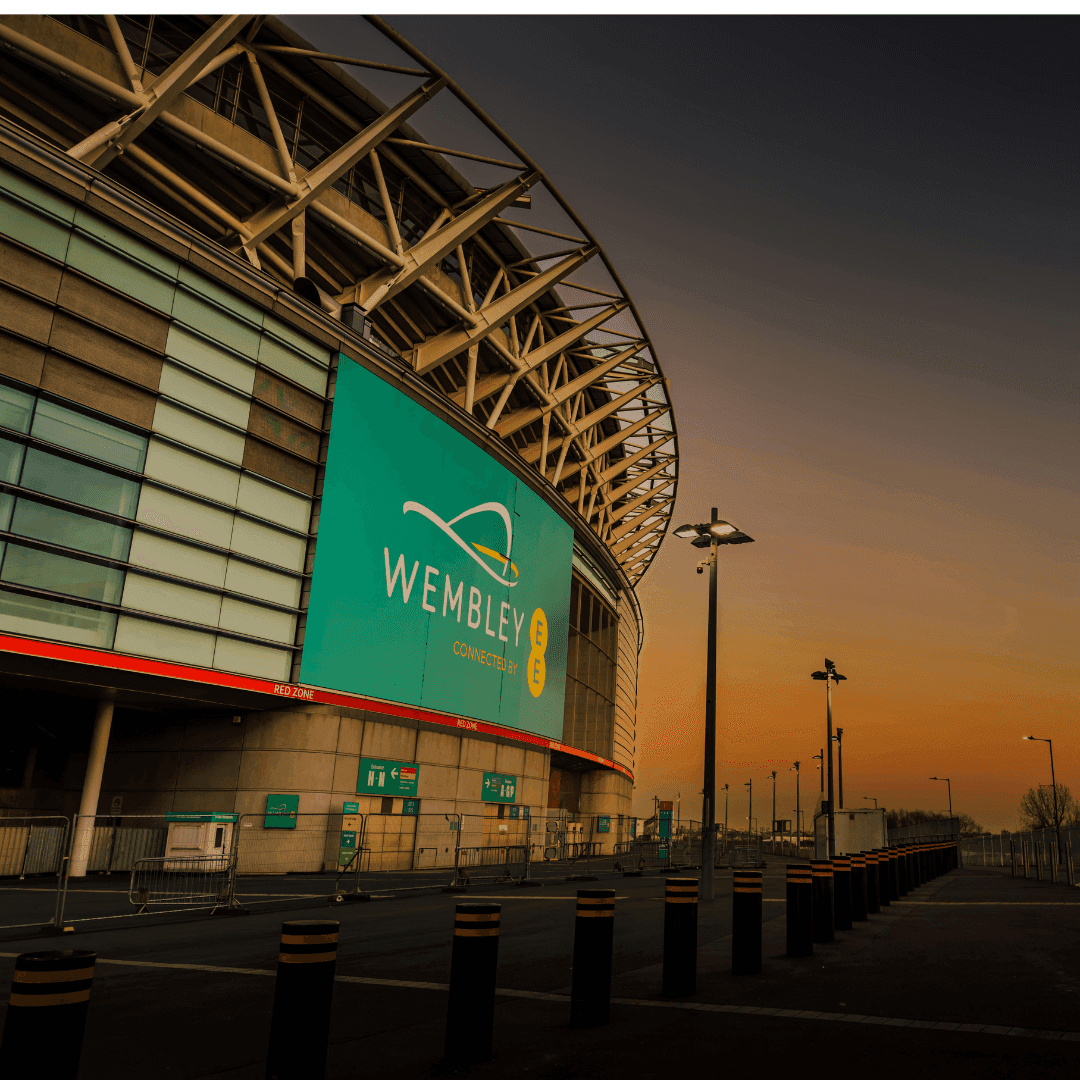Wembley Stadium exterior at sunset with illuminated signage and an empty parking lot in the foreground. - Home Instead