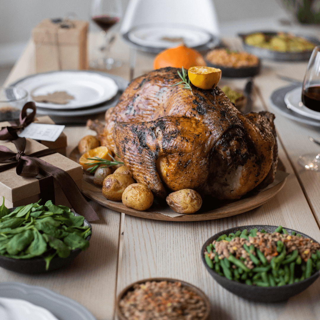 A roasted turkey with herbs and lemon on a dining table, surrounded by side dishes and gifts, ready for a festive meal. - Home Instead