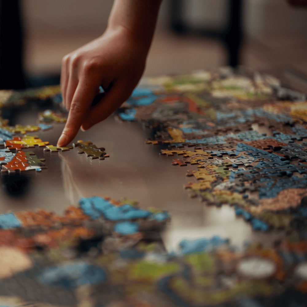 A hand placing a piece into a colorful jigsaw puzzle on a reflective surface. - Home Instead